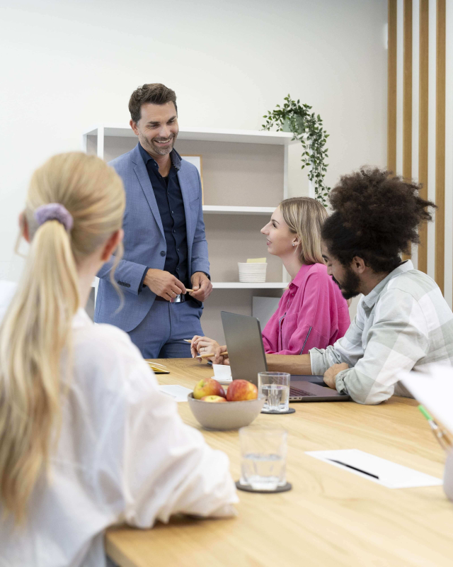Eine lachende Gruppe Kollegen sitzt im Konferenzraum am Tisch